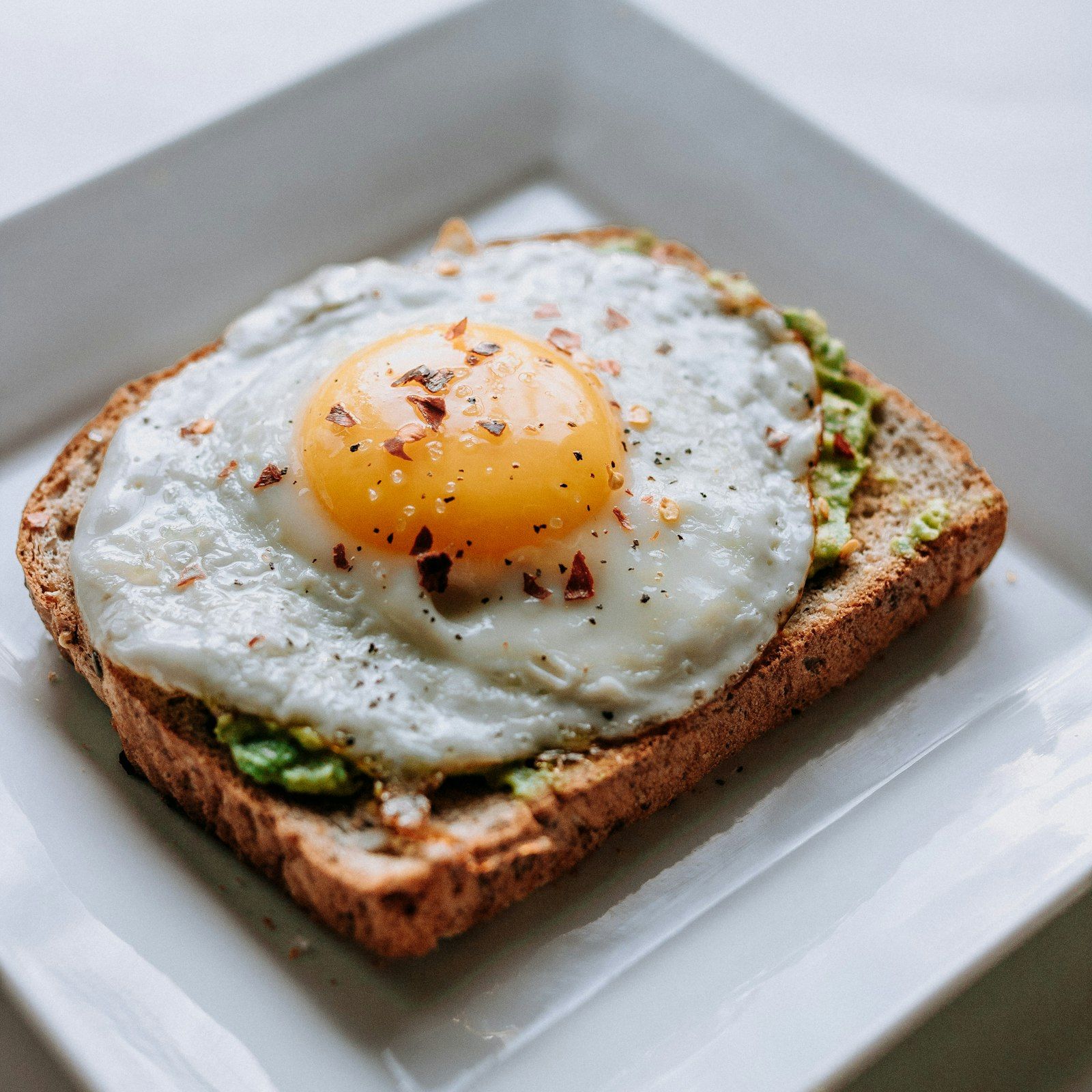Two slices of sourdough toast topped with smashed avocado and a halved poached egg, photographed from above on a linen napkin.