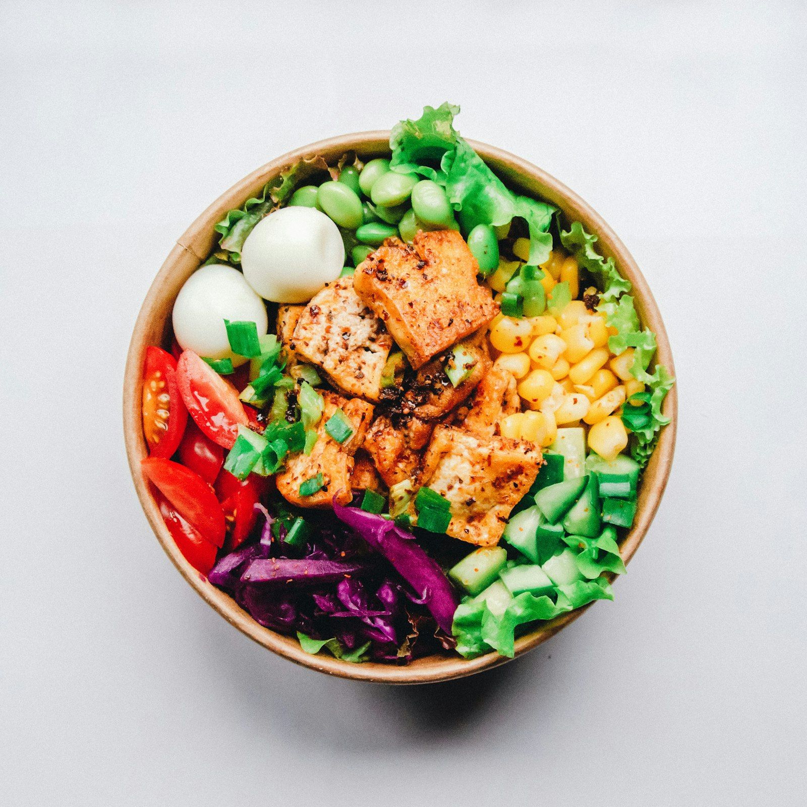 A bowl of mixed greens topped with sliced grilled chicken, red onion, and a lemon wedge.
